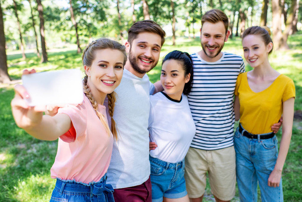 young smiling friends taking selfie on smartphone in park  - Fotografie, Obrázek
