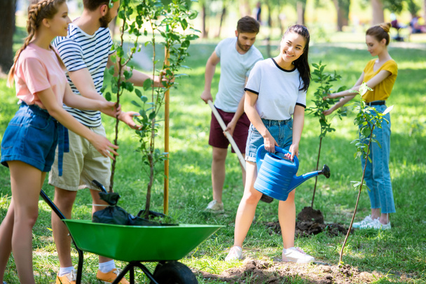 hymyilevät ystävät istuttavat uusia puita ja tekevät vapaaehtoistyötä puistossa yhdessä
 - Valokuva, kuva
