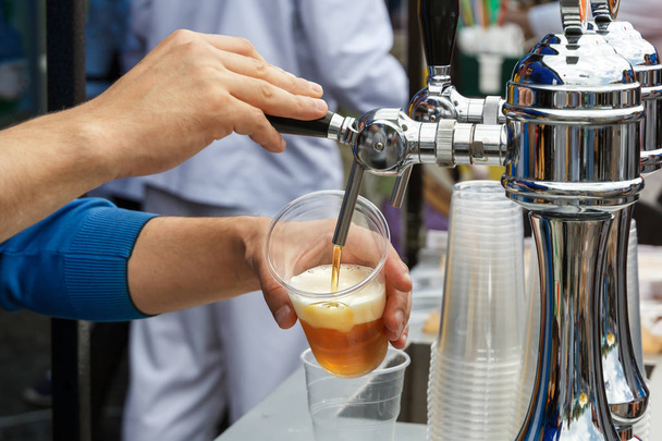 barman's hand holds a large glass in which fresh amber beer is poured with foam. Street trading - Photo, Image
