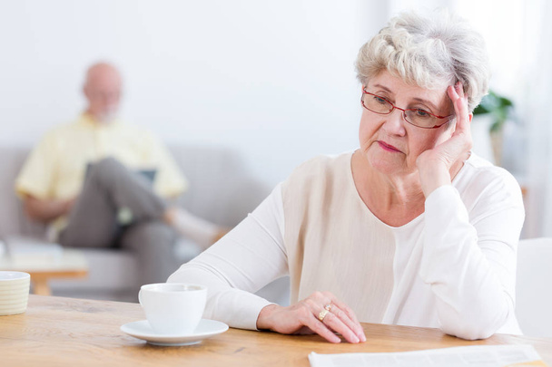 Sad elderly woman sitting at a wooden table, thinking about divorcing her husband - Photo, image