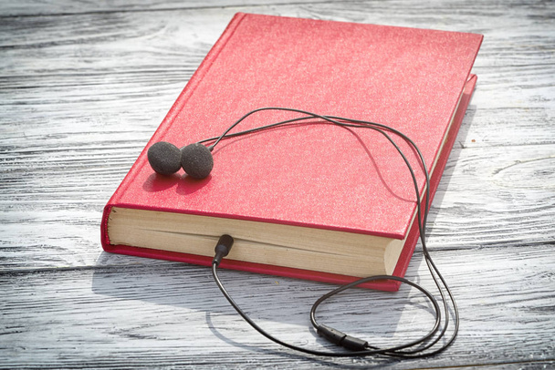 viejo libro rojo se encuentra en una mesa de madera con auriculares en ella y copiar el espacio para su texto. Concepto de audiolibro
. - Foto, imagen