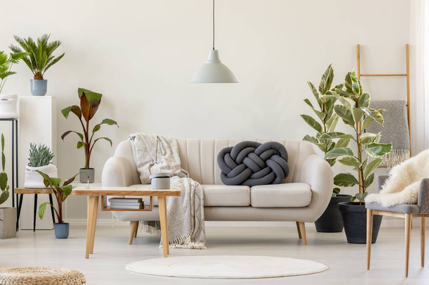 Wooden table in front of beige sofa in floral living room interior with plants. Real photo - Fotó, kép