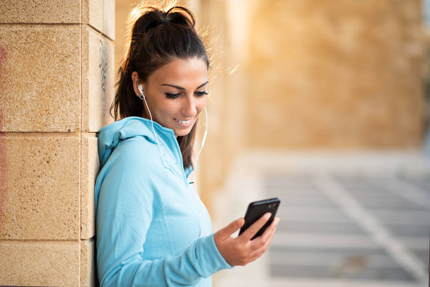 Young female brunette standing with cell phone and head set with hair pulled back - Photo, image