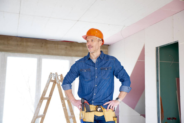 Portrait of thinking handyman standing with hand on his chin at the construction site.  - Photo, Image