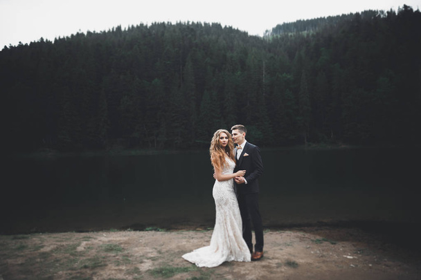 Young newly wed couple, bride and groom kissing, hugging on perfect view of mountains, blue sky - Fotografie, Obrázek