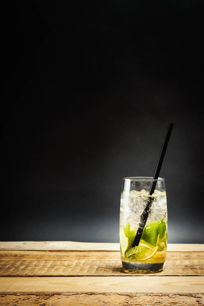 vaso de delicioso mojito con hojas de lima y menta sobre una mesa de madera sobre un fondo negro
 - Foto, Imagen
