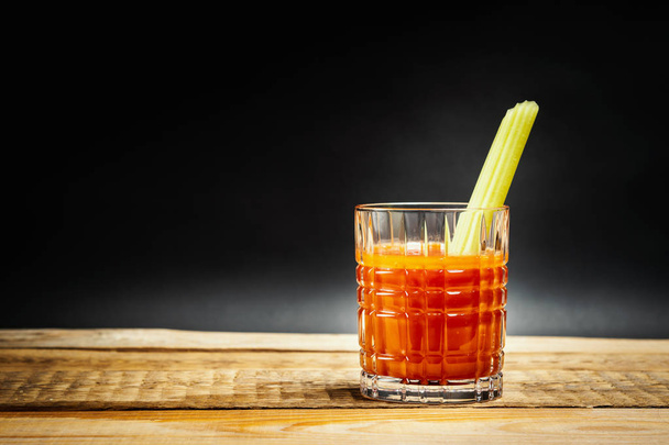 ζουμερό κόκκινο ποτό bloody mary με ένα κομμάτι πράσινο σέλινο σε ένα ξύλινο τραπέζι - Φωτογραφία, εικόνα