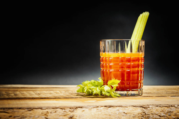 juicy red drink bloody mary with a piece of green celery on a wooden table - Photo, Image