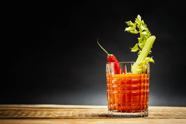 ζουμερό κόκκινο ποτό bloody mary με ένα κομμάτι πράσινο σέλινο και τις πιπεριές τσίλι σε ένα ξύλινο τραπέζι - Φωτογραφία, εικόνα