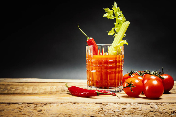 ζουμερό κόκκινο ποτό bloody mary με ένα κομμάτι πράσινο σέλινο και τις πιπεριές τσίλι και τις ντομάτες σε ένα ξύλινο τραπέζι - Φωτογραφία, εικόνα