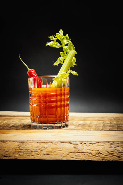 juicy red drink bloody mary with a piece of green celery and chilli peppers on a wooden table - Photo, Image