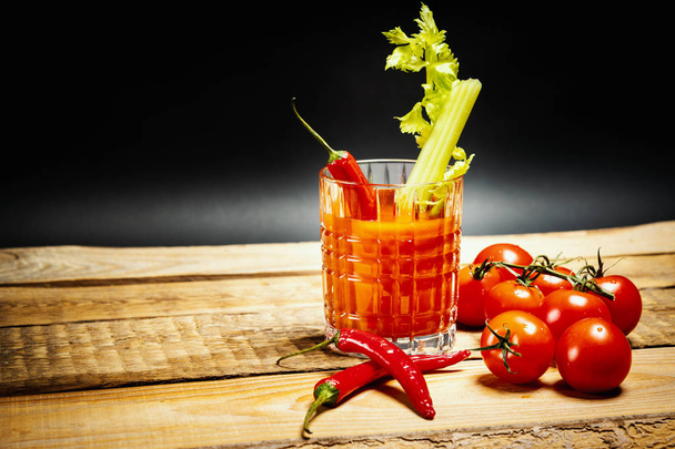 木製テーブルの上のトマトと唐辛子緑色のセロリの部分とジューシーな赤い飲み物ブラッディマリー - 写真・画像
