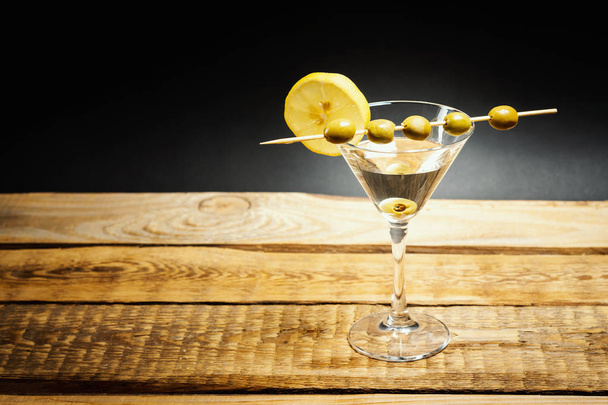 delicious martini drink in a glass with olives on a stick and lemon on a wooden table - Photo, Image