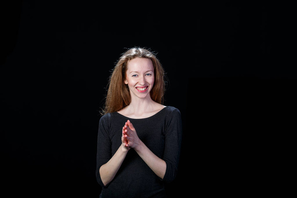 Joyful young red-haired girl rubs his palms against a black background - Photo, image