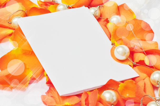 Folha de papel branco sobre pétalas laranja de rosas e pérolas
 - Foto, Imagem
