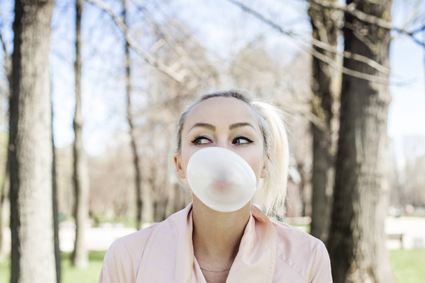 Cute young woman with bubble chewing gum outdoors, lifestyle portrait - Photo, image