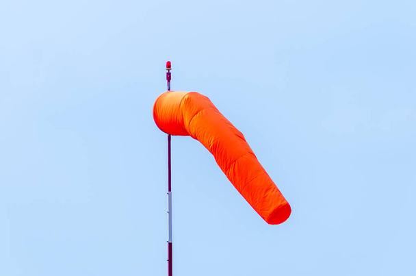 Un calzino a vento da campo d'aviazione arancione su un palo bianco e rosso con un faro rosso in alto appeso in una leggera brezza con un cielo blu senza nuvole dietro
 - Foto, immagini