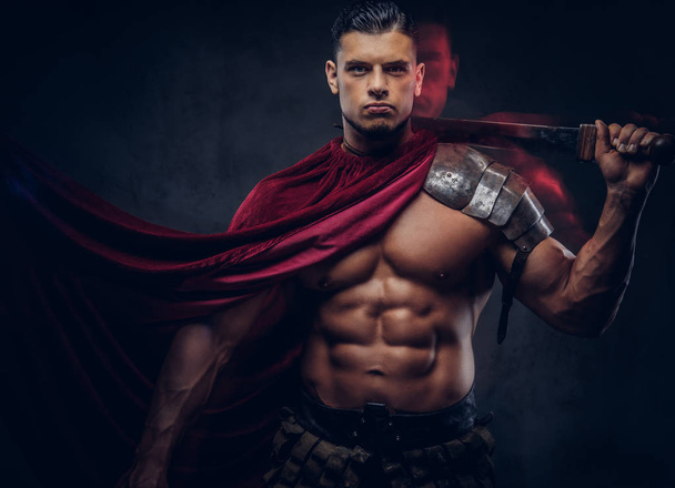 Жестокий греческий воин с мускулистым телом в боевой форме, позирующий на тёмном фоне
. - Фото, изображение