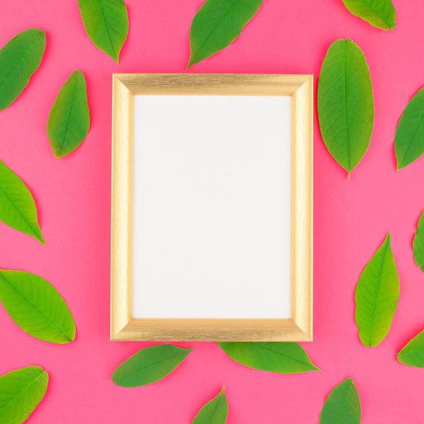 Creative flat lay top view pattern with fresh green leaves on bright pink square background with golden frame mock up and copy space in minimal pop art style, template for text - Foto, afbeelding