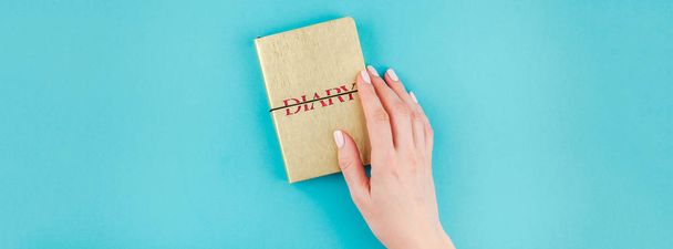 Long wide banner of woman hands holding small golden notebook diary with copy space on turquoise paper background in minimalism style. Template for feminine blog, social media - Photo, Image
