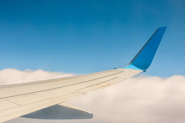 Ala de un avión volando por encima de las nubes sobre fondo azul del cielo
 - Foto, Imagen