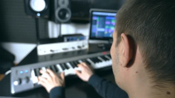 Male musician playing at synthesizer at sound recording studio. Man plays solo of music. Fingers of pianist at the piano keys. Beautiful background of workplace. Slow motion Rear back view - Footage, Video