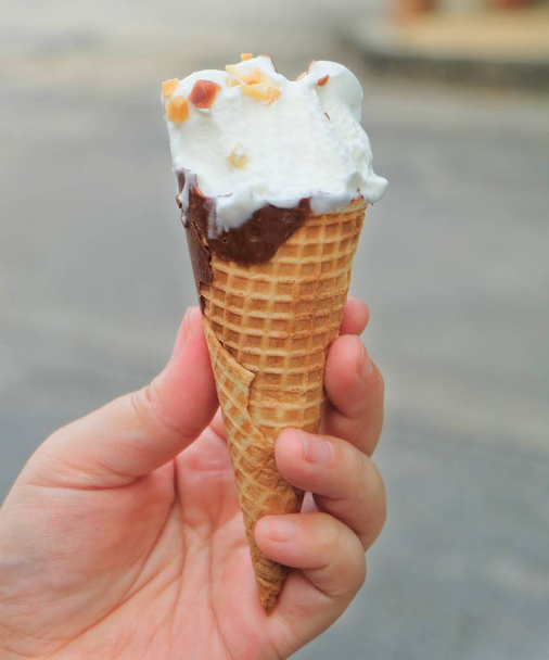 Hand Holding Vanilla Ice Cream with Chocolate and Nut in A Waffle Cone. - Photo, Image