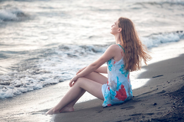 Beautiful girl sits on a sandy beach on the seashore. - Foto, Imagem