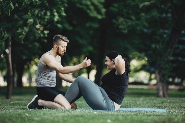 Trainer assisting overweight woman doing sit-ups - Fotoğraf, Görsel