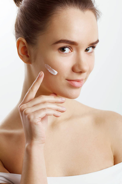 Skin care. Beautiful Woman putting face cream. Attractive brunette girl on grey backgrou - Fotoğraf, Görsel