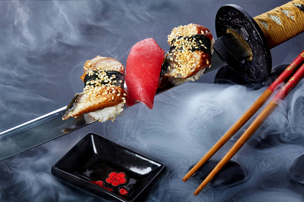 Close up of sushi set with chopsticks .Sashimi.Nigiri. On katana sword with fog .Creative shot. Japanese athmophere. - Fotografie, Obrázek