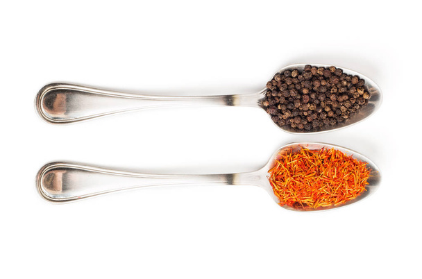 Diferentes especias en cucharas de hierro aisladas sobre fondo blanco. Peppercorns negros secos y azafrán. Vista desde arriba
. - Foto, Imagen