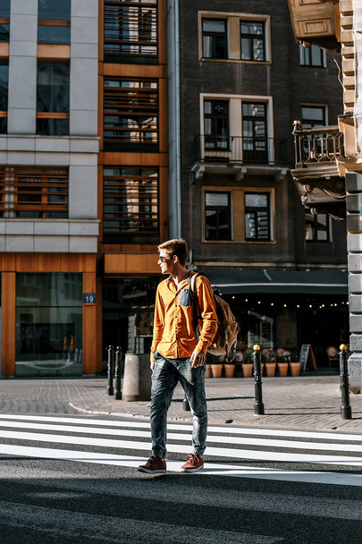 A srác áthalad át a gyalogos átkelés az utcán. Ízlésesen felöltözött férfi táskát tanulni és dolgozni siet. Az ember utazik a városokat. Európa. Lengyelország, Varsó. - Fotó, kép