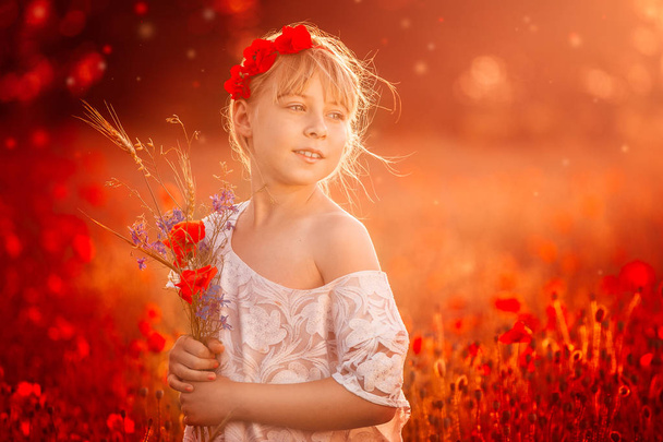 Κινηματογράφηση σε πρώτο πλάνο της ένα χαριτωμένο κορίτσι σε πεδίο παπαρούνας λουλούδια στον ανοιχτό αέρα. Το κορίτσι με τις παπαρούνες. Μικρό κορίτσι με τα ξανθά μαλλιά και μια λευκή μπλούζα στέκεται σε ένα πεδίο παπαρούνας με ένα μπουκέτο λουλούδια - Φωτογραφία, εικόνα