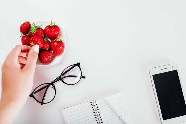 Top view of student 's desktop with notebook, smartphone, glasses and strawberries. Учиться и перекусить. Рабочее пространство
 - Фото, изображение