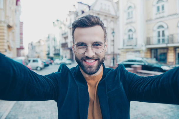 Retrato de homem atraente alegre disparando selfie na câmera frontal com duas mãos enquanto caminhava sobre o fundo da rua. Turismo turismo viagem viajante conceito
 - Foto, Imagem