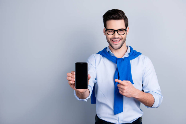 Portrait with copy space of attractive man with blue pullover tied around the neck recommend doing online shopping,  presenting, indicating with forefinger on smart phone over grey background - Photo, Image