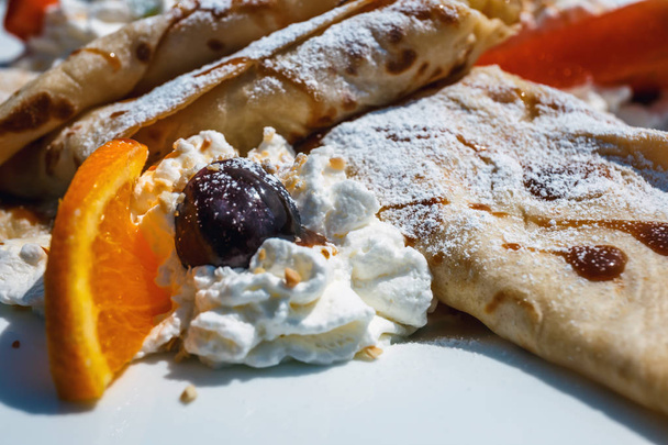 panqueque con relleno de manzana decorado con crema batida, fresas y naranjas
 - Foto, Imagen