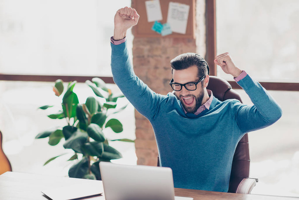 Stunning, smart, lucky, yelling man with raised arms, celebrating successfully completed work, project, presentation, sitting on armchair at desk in work station - Foto, imagen