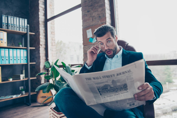 Portrait of surprised smart funny funky bearded intelligent curious handsome chief wearing smart suit old-fashioned jeans touching glasses reading news from newspaper at workplace - Foto, Imagem