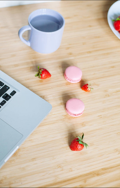 Workplace with laptop,  macaroons, strawberry and cup of tea on the table - Foto, Imagem