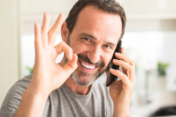 Homem de meia idade usando smartphone fazendo sinal ok com os dedos, excelente símbolo
 - Foto, Imagem
