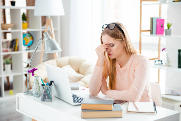 Portrait of sad upset girl feeling unwell bad suffering from head ache keeping eyes closed sitting at desk in modern room with interior indoor preparing for lesson. Self development concept - Foto, Bild