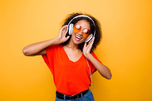 Portrait of cheerful positive woman having headphones on head listening favorite club music singing song dancing isolated on yellow background - Foto, Imagen