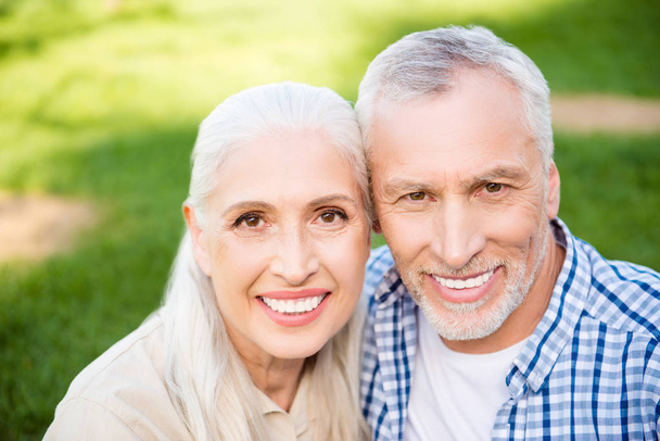 Head shot portrait of sweet cute grandma and granddad resting outdoor in park looking at camera over blurred background - Photo, image