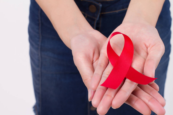 woman hand holding red ribbon bow, hiv or aids awareness symbol presented by woman in studio shot. medical, charity, fund raising concept for red ribbon hiv aids day awareness - 写真・画像
