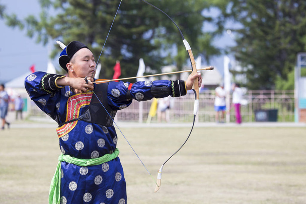 Competitions in shooting from a sports bow in Siberia. Mongolian competitions in archery. The sportsman is dressed in a traditional Buryat-Mongolian suit, shooting with his arrows during a national holiday. - Photo, Image