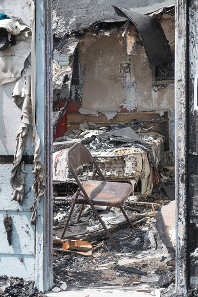 Kijk door de deur naar een burn-out slaapkamer met een matras en klapstoel - Foto, afbeelding
