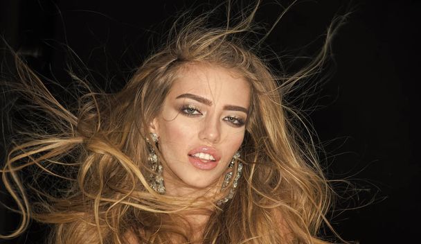sexy fashion woman. Hot sexy girl. Woman with long hair and sensual lips looks attractive. Fashionable sexy girl with makeup, lipstick, mascara, wears in sparkling big earrings jewelry, dark - Zdjęcie, obraz
