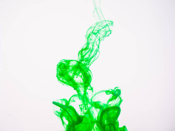 Green acrylic colour dissolving into water, close up view. Abstract green coloured background. Acrylic paint dropped into water and photographed while in motion. Droplet of color on white background. - Foto, Bild
